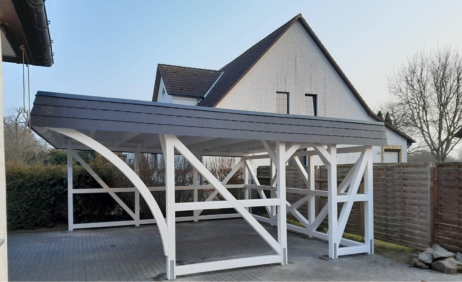 Fachwerkcarport aus weiß lackiertem Fichtenholz mit grauem Schieferdach. Hier Seitenansicht von rechts.