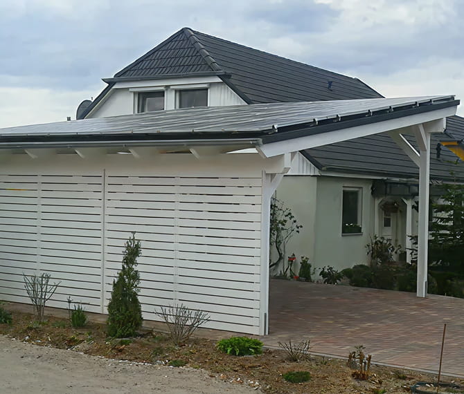 Ein modernes Haus mit dunklem Ziegeldach in Berlin hat einen weißen Holzcarport und eine gepflasterte Auffahrt mit minimaler Vorgartengestaltung.